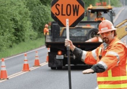 A man holding up a slow sign while standing in front of a dump truck.