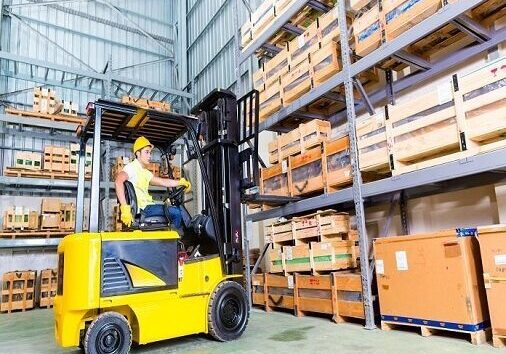 A man in yellow vest riding on the back of a forklift.
